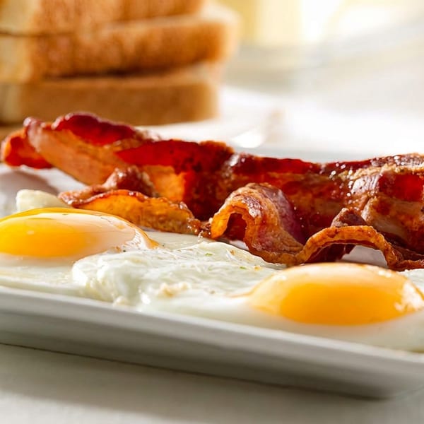 A breakfast plate with two fried eggs, crispy bacon, toast, and orange juice.